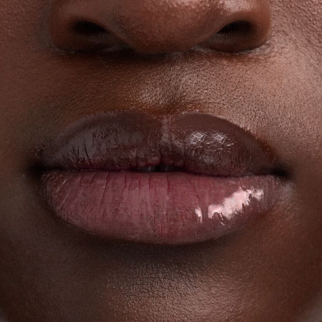 Deep skin tone model wearing Wet Lip Oil Gloss in Cola