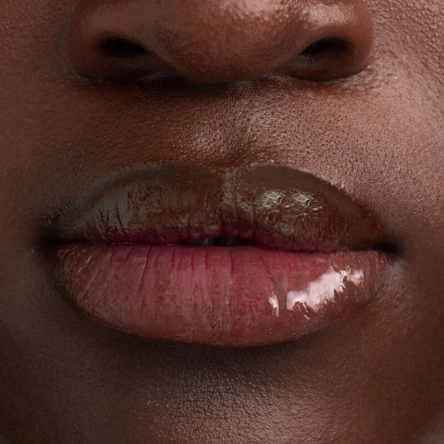 Deep skin tone model wearing Wet Lip Oil Gloss in Grapesicle